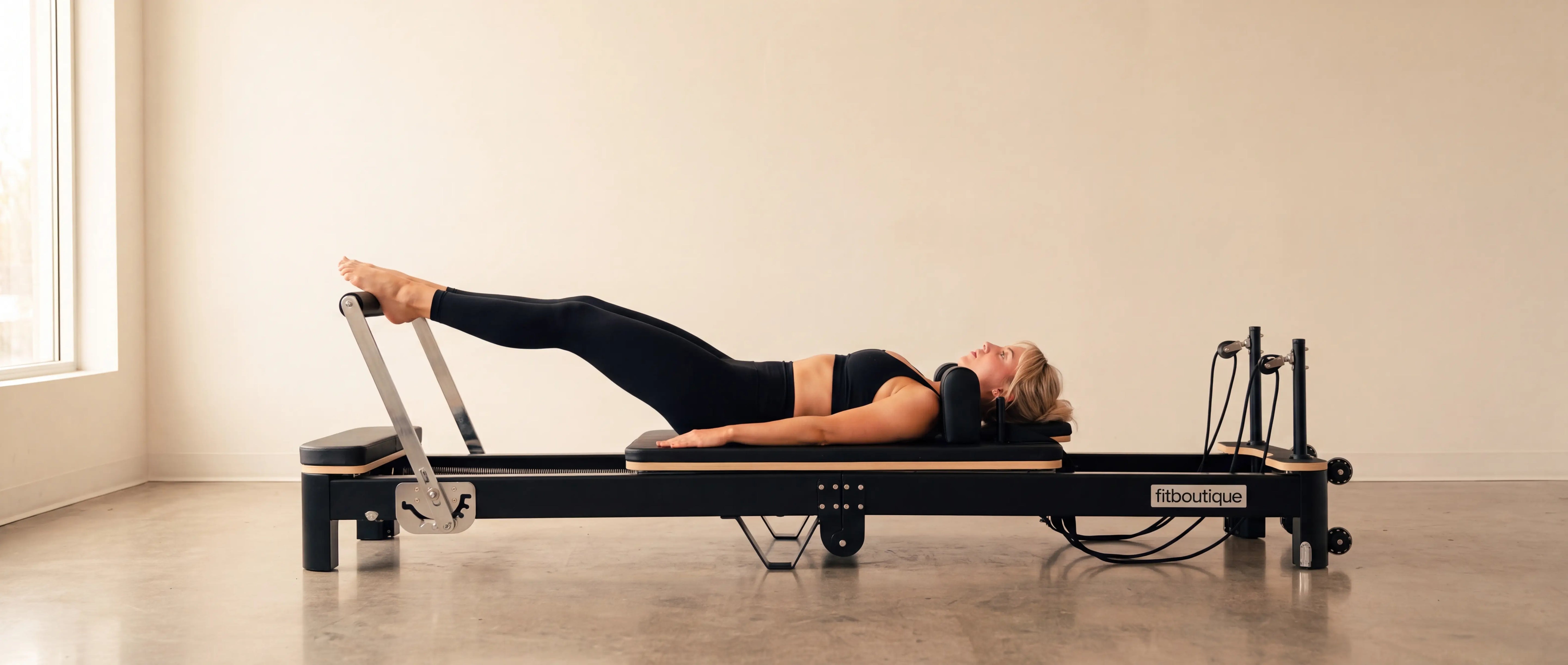 Woman doing reformer Pilates at home on the FitBoutique Ivory reformer