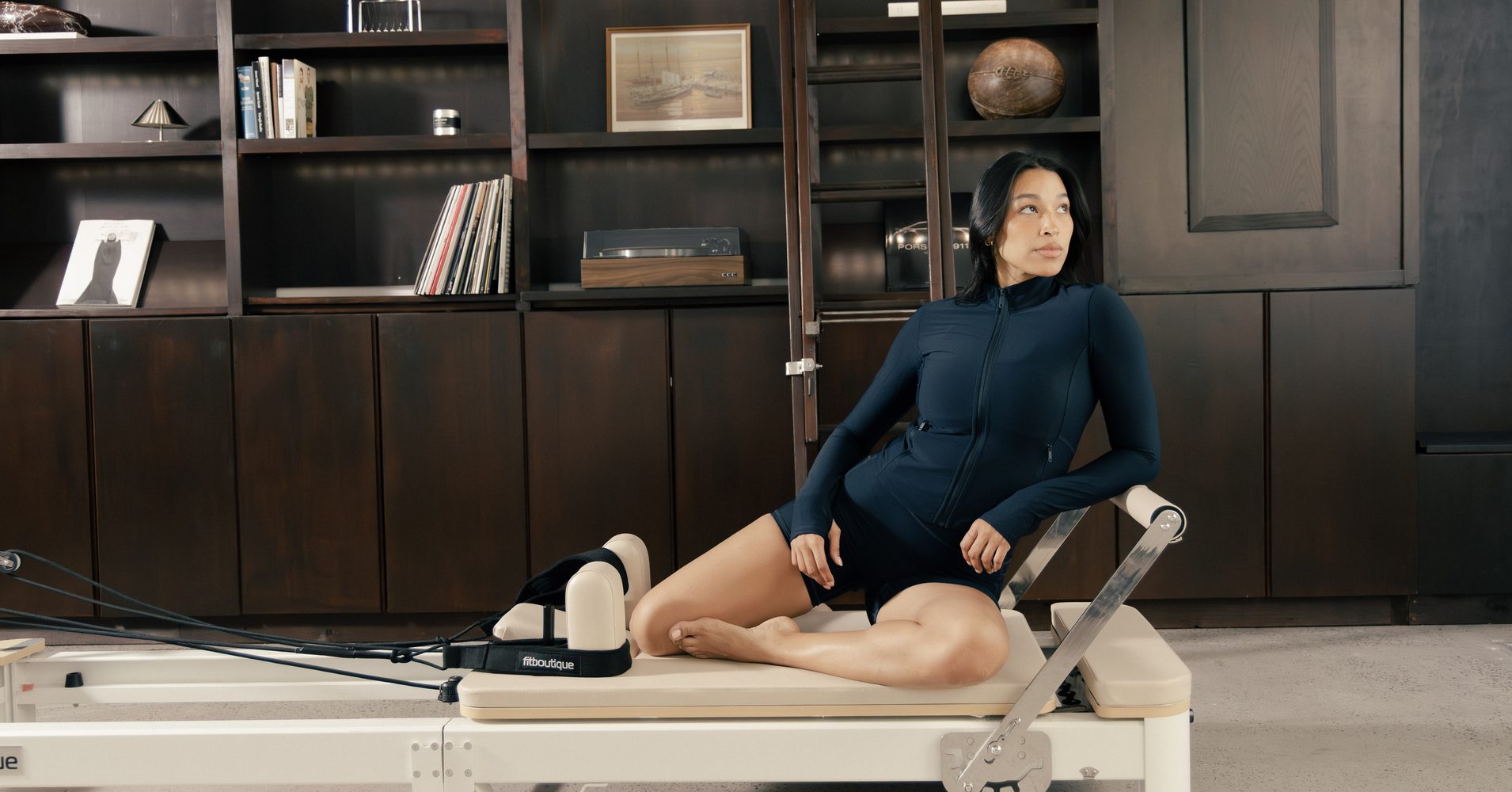 Woman seated on a FitBoutique reformer carriage in a dark timber studio