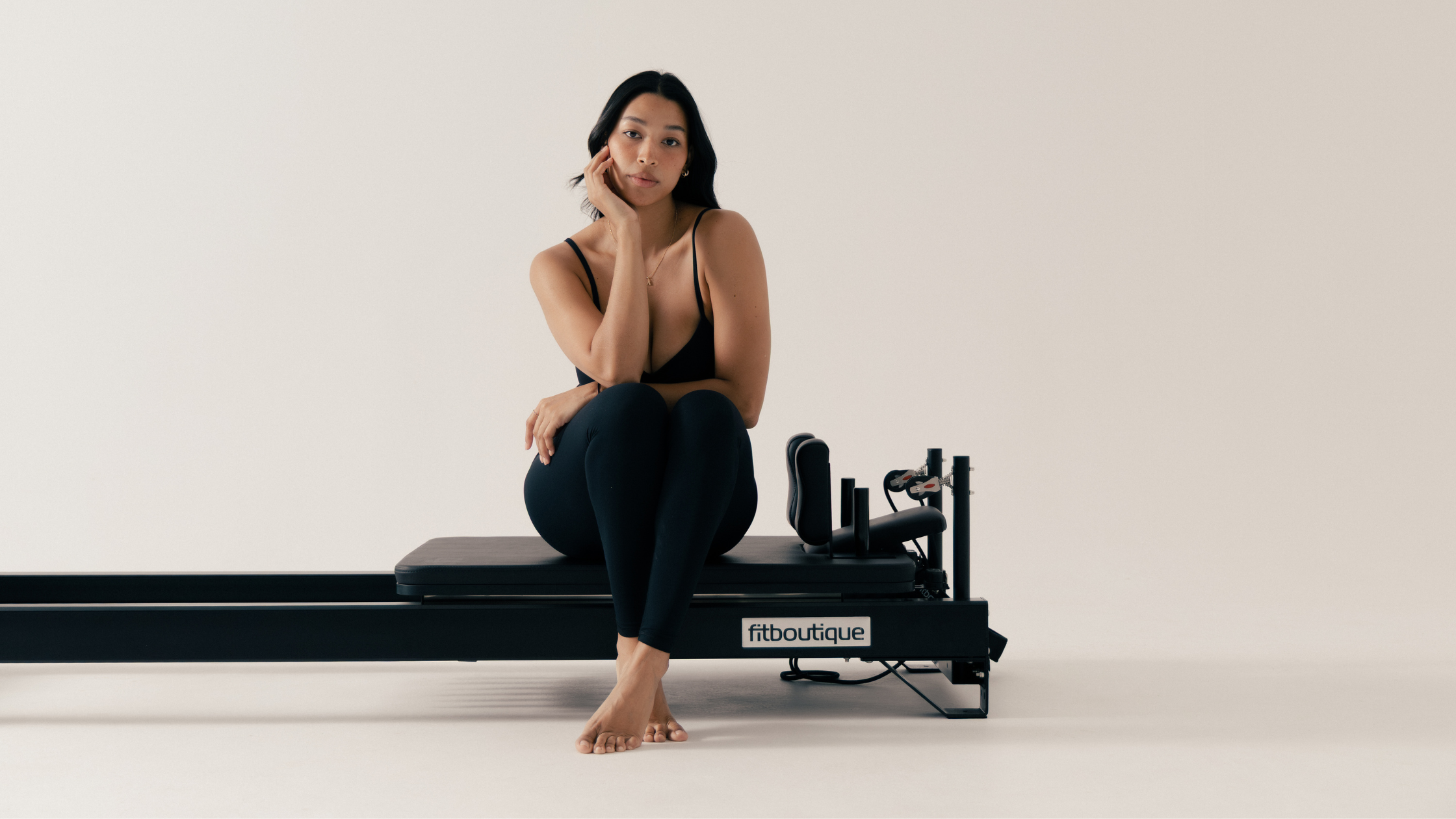 Woman seated comfortably on a FitBoutique reformer in a studio