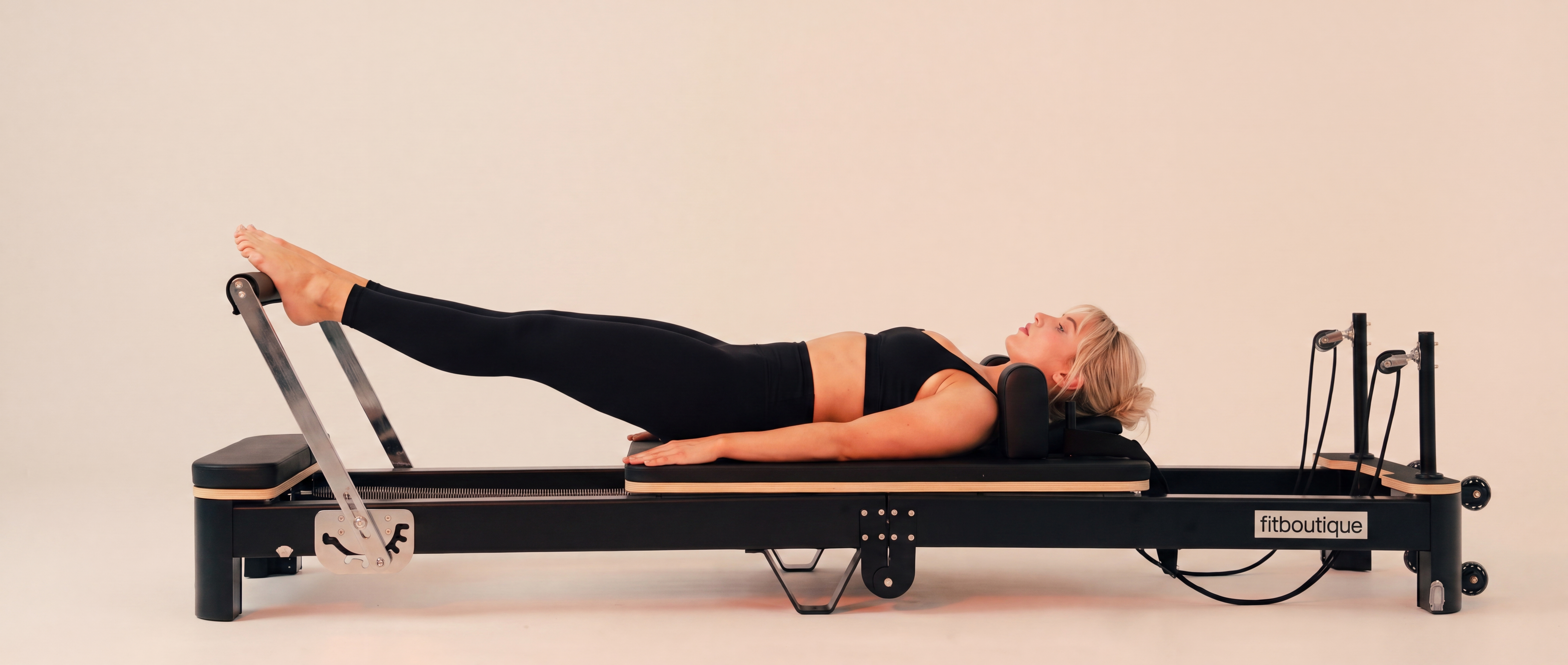 Woman doing a beginner reformer Pilates workout on the FitBoutique Ivory reformer